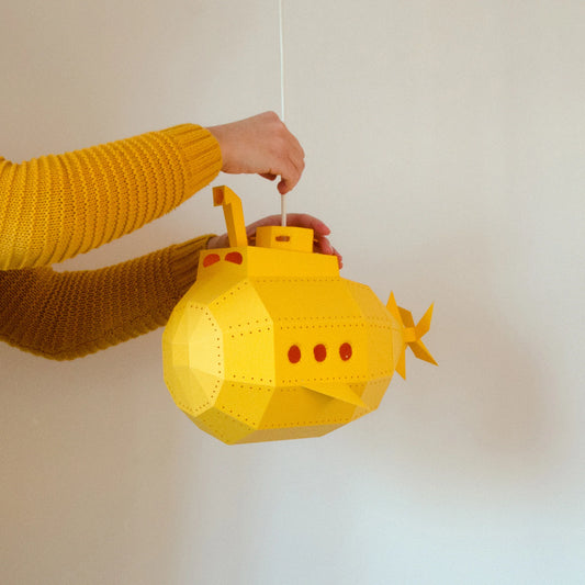 Pessoa a segurar o submarino de papel amarelo montado do kit candeeiro DIY.