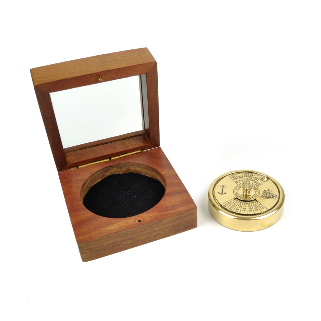 Calendário perpétuo circular em latão dourado polido da Loja do Museu de Marinha, mostrando o disco mecânico de 100 anos com gravações de uma caravela e de uma âncora.