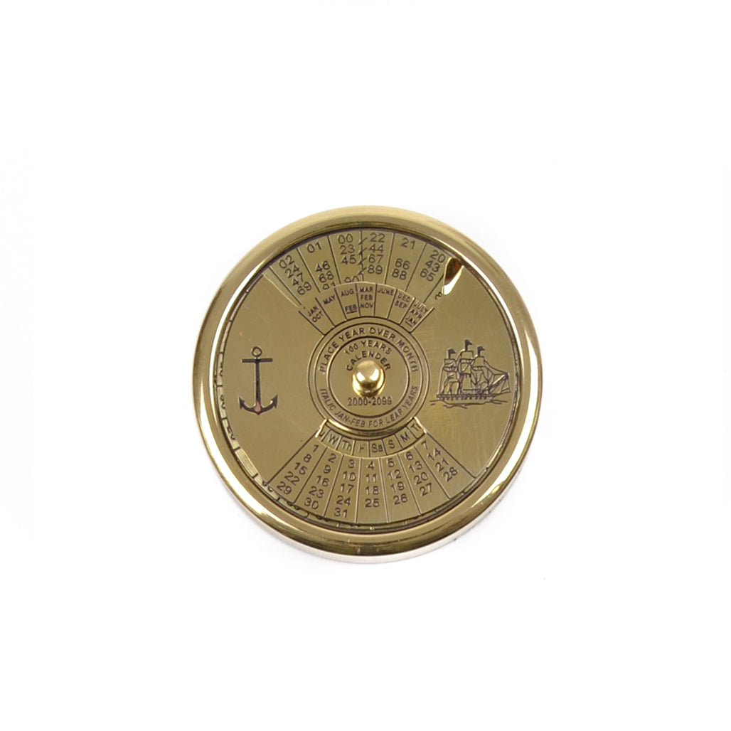 Calendário perpétuo circular em latão dourado polido da Loja do Museu de Marinha, mostrando o disco mecânico de 100 anos com gravações de uma caravela e de uma âncora.