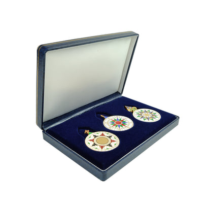 Estojo rígido azul-marinho aberto, revelando o berço de veludo escuro com o conjunto das três medalhas da Rosa dos Ventos encaixadas, da Loja do Museu de Marinha.