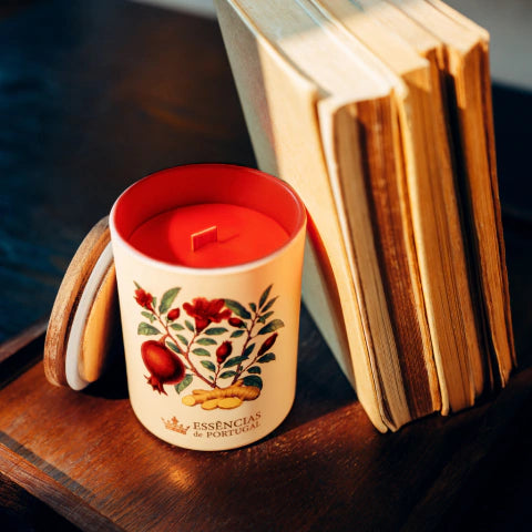 Vela aromática Flor de Romãzeira e Gengibre em copo ilustrado com tampa de madeira junto a livros clássicos