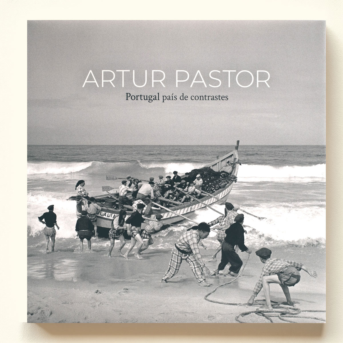 Capa do livro "Artur Pastor - Portugal país de contrastes" exibindo uma icónica fotografia histórica a preto e branco de pescadores portugueses na praia a puxar um barco de pesca artesanal.