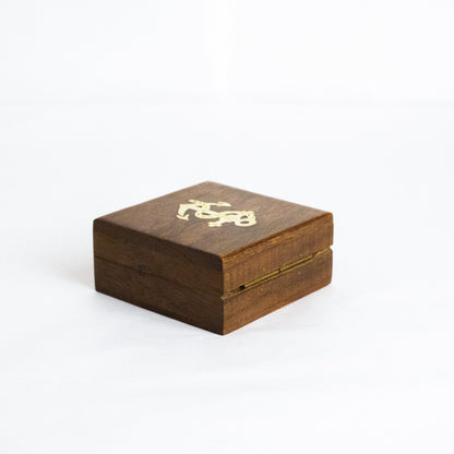 Caixa de madeira nobre fechada da bússola decorativa, destacando o topo liso com o embutido metálico dourado em forma de âncora náutica.