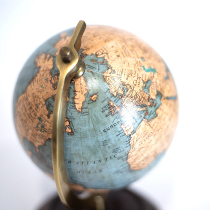 Pormenor de globo terrestre clássico compacto de 18cm de altura sobre base de madeira e suporte de latão dourado, com cartografia detalhada em tons ocre e azul suave.