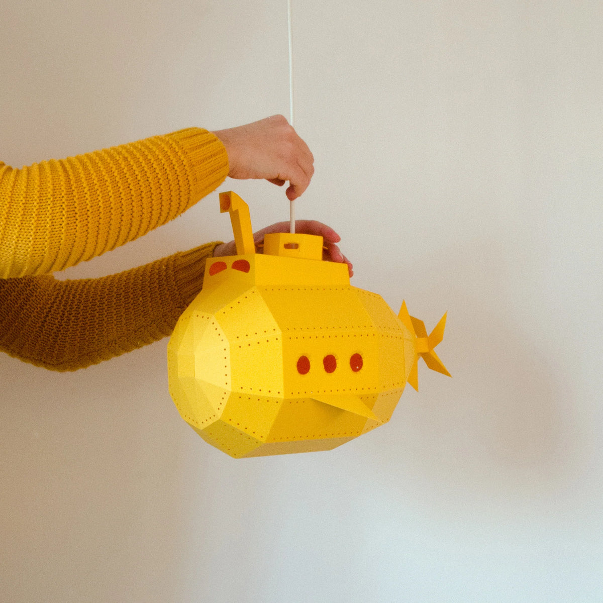 Pessoa a segurar o submarino de papel amarelo montado do kit candeeiro DIY.