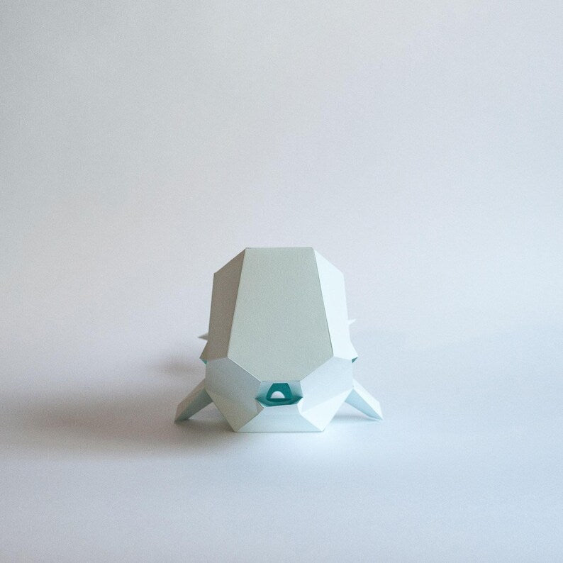 Candeeiro decorativo de papel em formato de baleia cachalote com design geométrico moderno aceso, emitindo uma luz suave sobre uma superfície plana.
