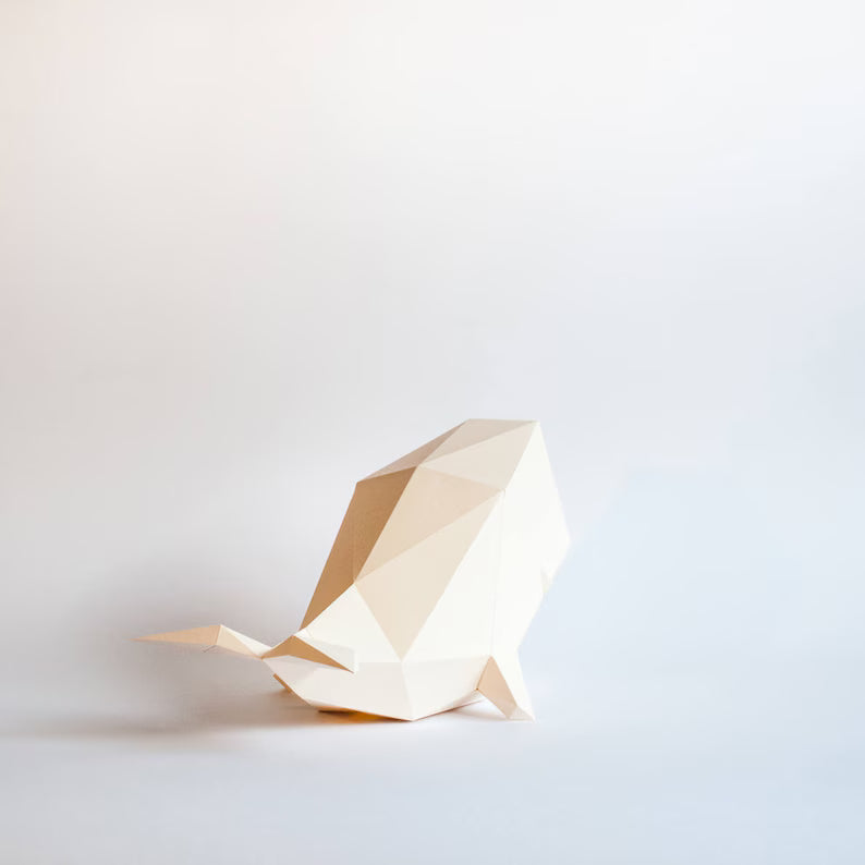 Candeeiro decorativo de papel em formato de baleia cachalote com design geométrico moderno aceso, emitindo uma luz suave sobre uma superfície plana.