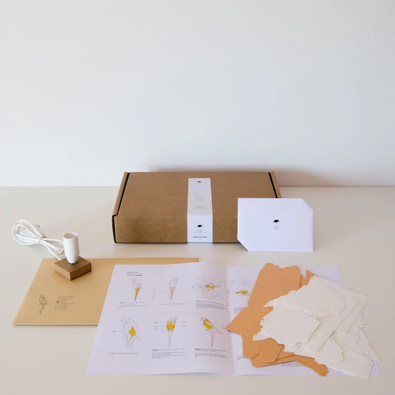 Candeeiro decorativo geométrico de papel em formato de papagaio tropical aceso sobre uma mesa, emitindo uma luz quente e realçando o design papercraft.