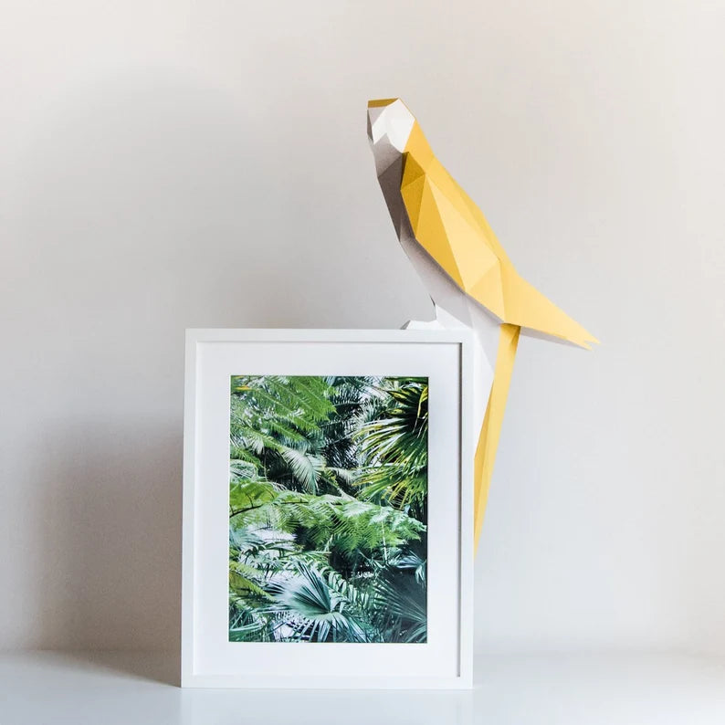 Candeeiro decorativo geométrico de papel em formato de papagaio tropical aceso sobre uma mesa, emitindo uma luz quente e realçando o design papercraft.