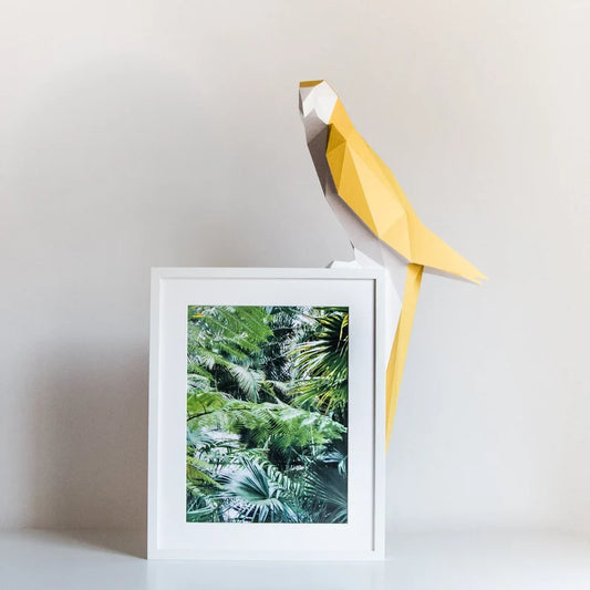 Candeeiro decorativo geométrico de papel em formato de papagaio tropical aceso sobre uma mesa, emitindo uma luz quente e realçando o design papercraft.